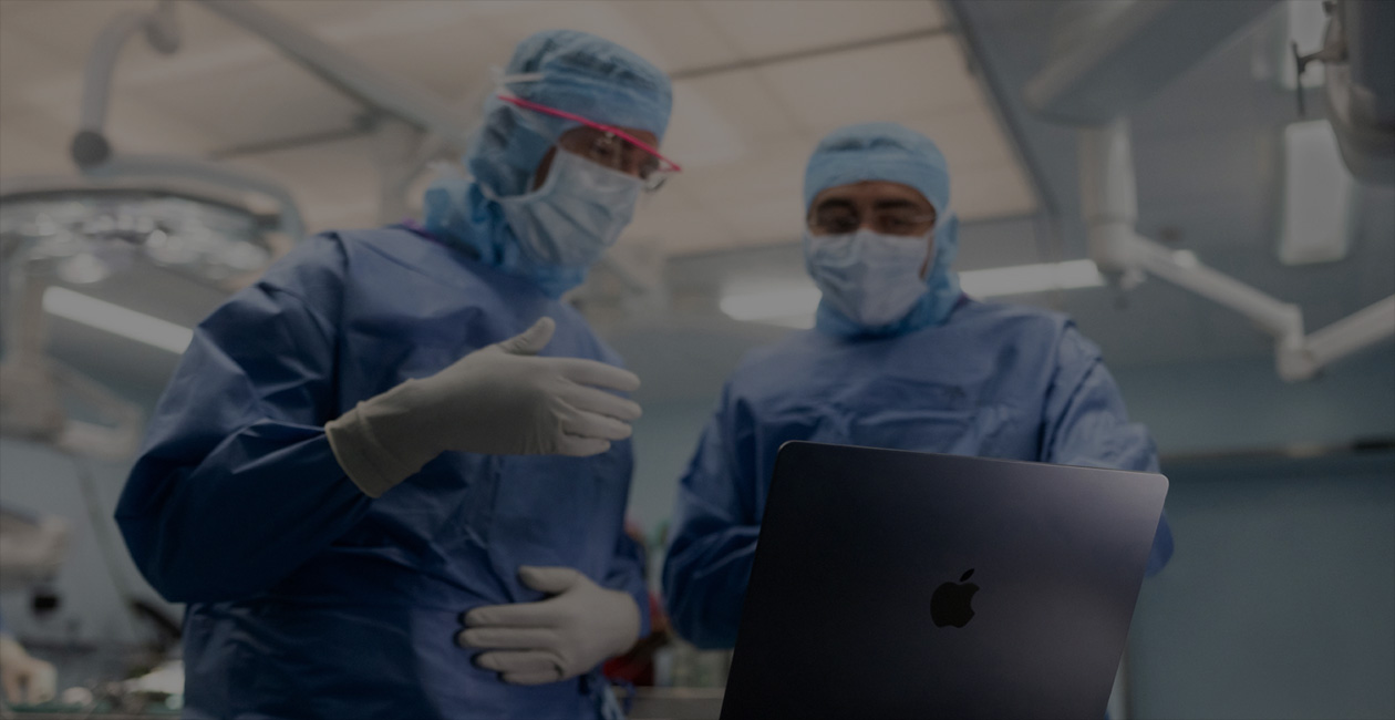To kirurger i operationstøj kigger på en MacBook Pro på operationsstuen.